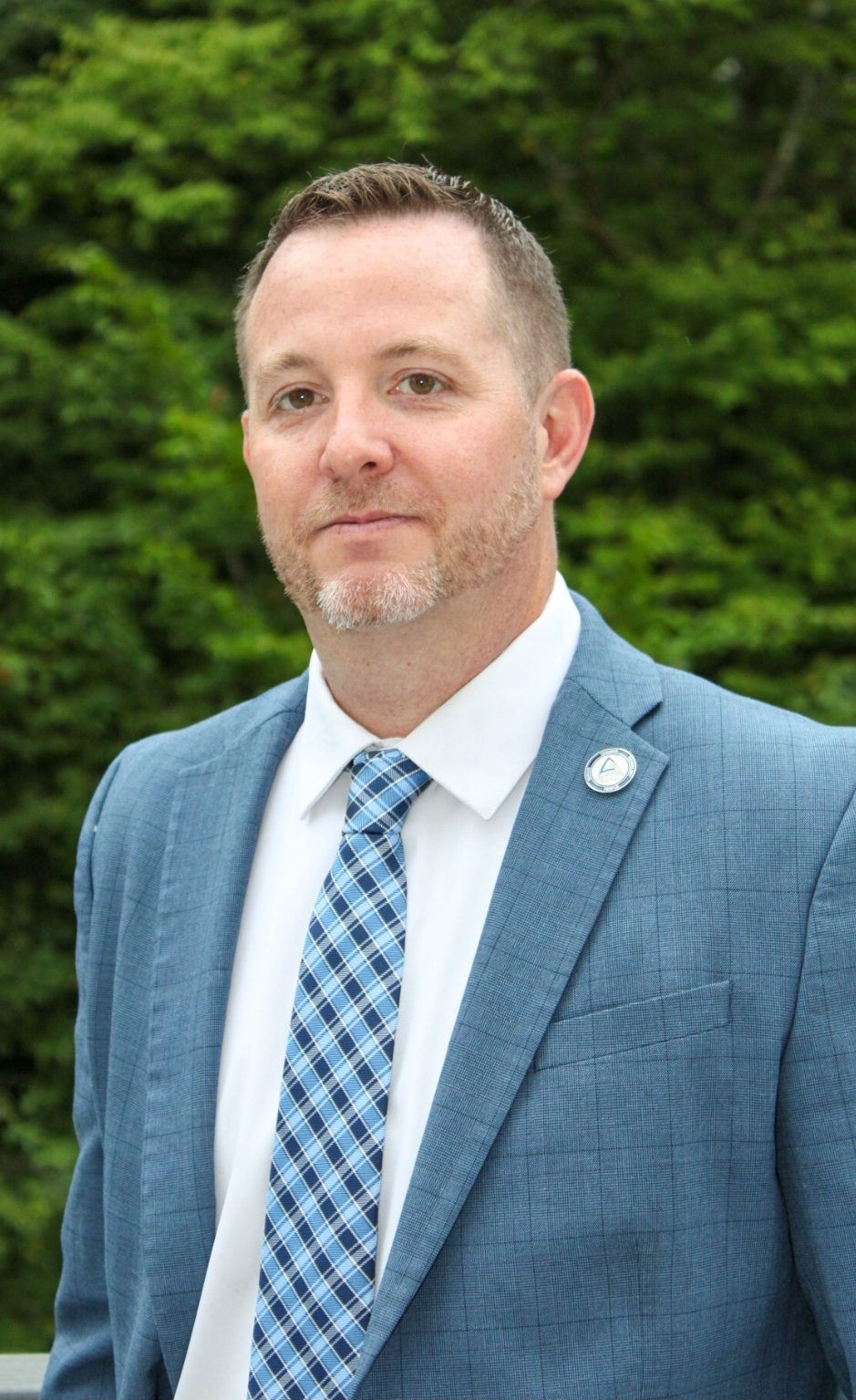 Man in a blue suit with a checkered tie standing outdoors.